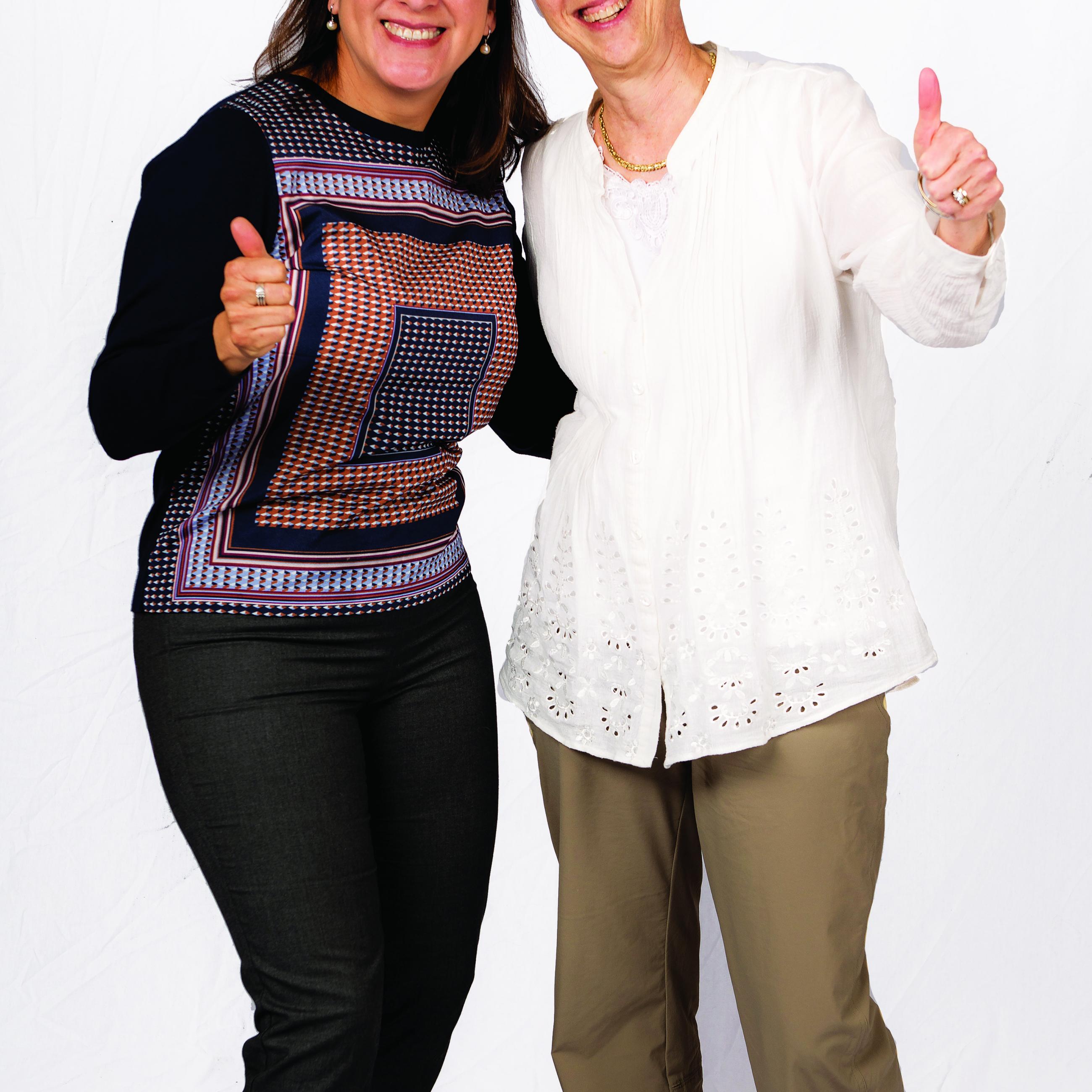 Two women pose with their thumbs up in front of the camera.