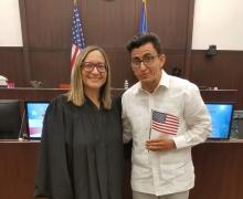 An immigration judge and new citizen holding an American flag in an immigration courtroom.
