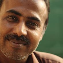 A man smiling in front of a green background.