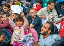 A girl standing in a crowd of people holding a sign that reads "SOS"